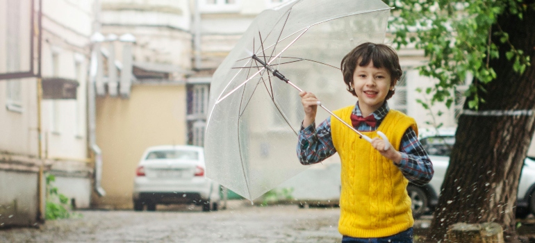 A young boy playing outside in the rain holding an umbrella.