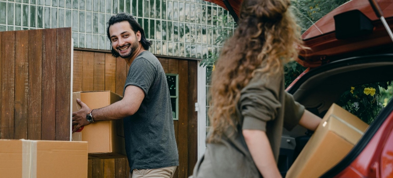 A smiling couple is unloading boxes from a car 