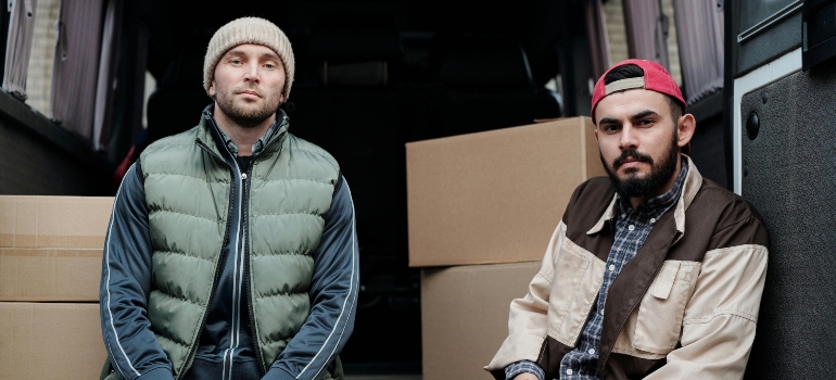 Two men in the jacket and caps are sitting in the back of the van.